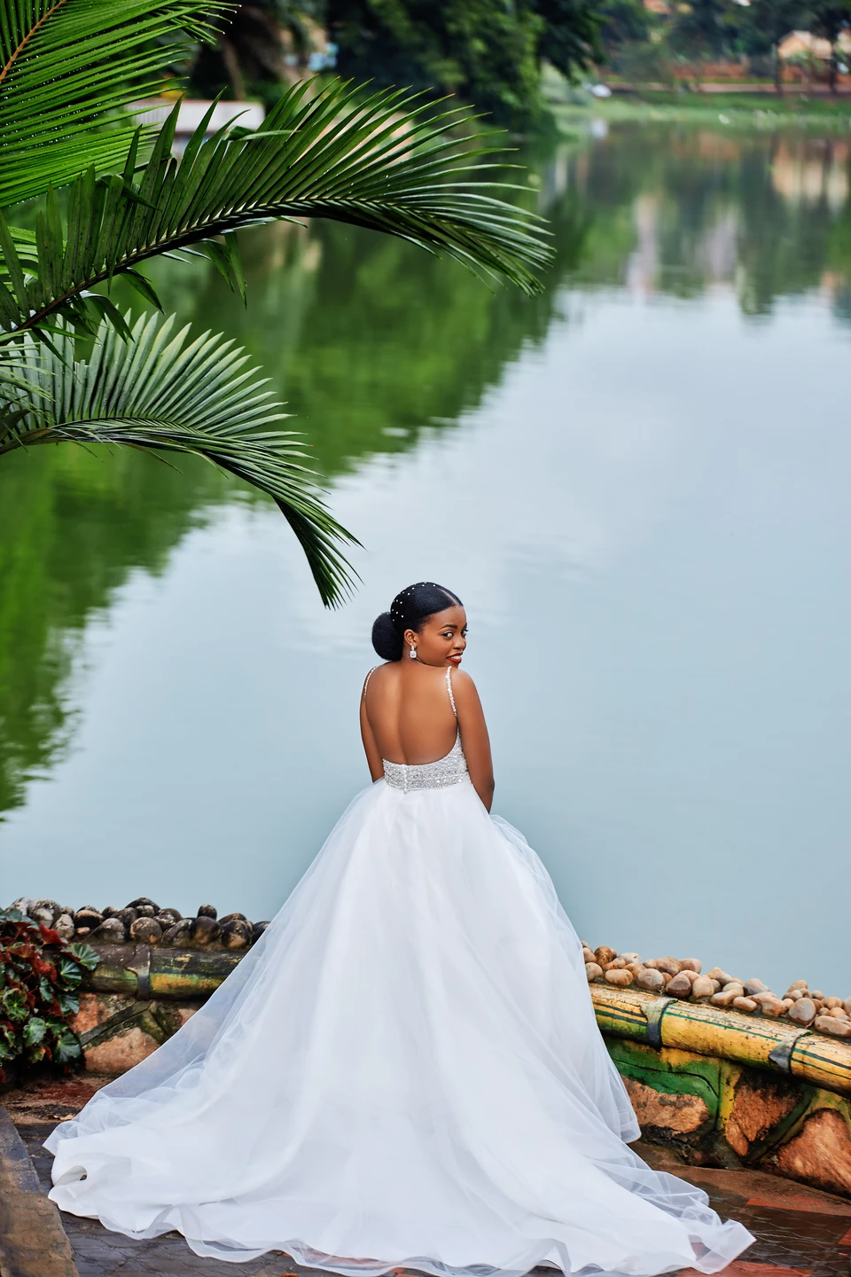 Bride in her wedding dress under palms beside a lake